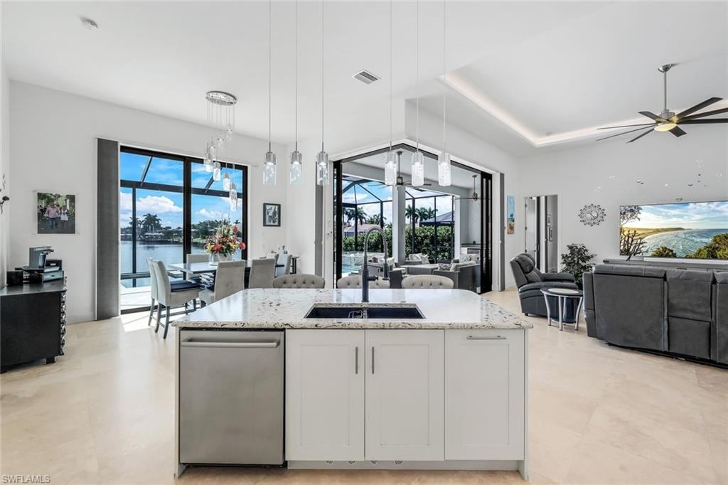 Kitchen with white cabinetry, light stone counters, hanging light fixtures, dishwasher, and a center island with sink