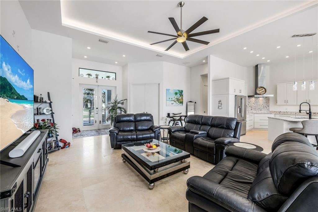 Living area with a tray ceiling, a high ceiling, ceiling fan, french doors, and recessed lighting