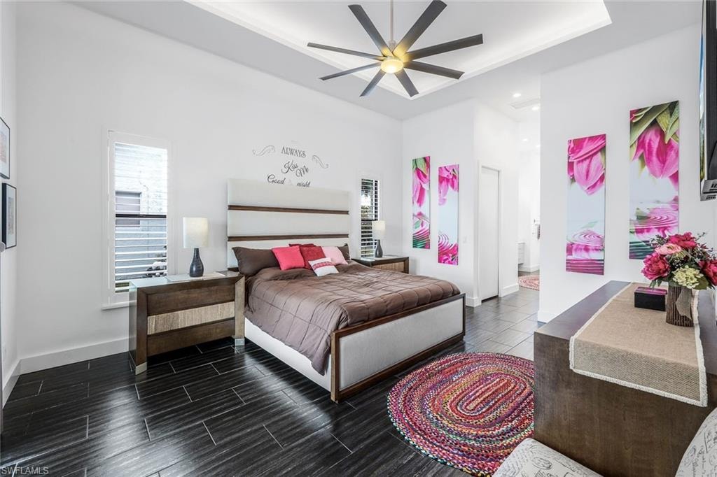 Bedroom featuring a raised ceiling, a ceiling fan, wood finish floors, ensuite bath, and recessed lighting