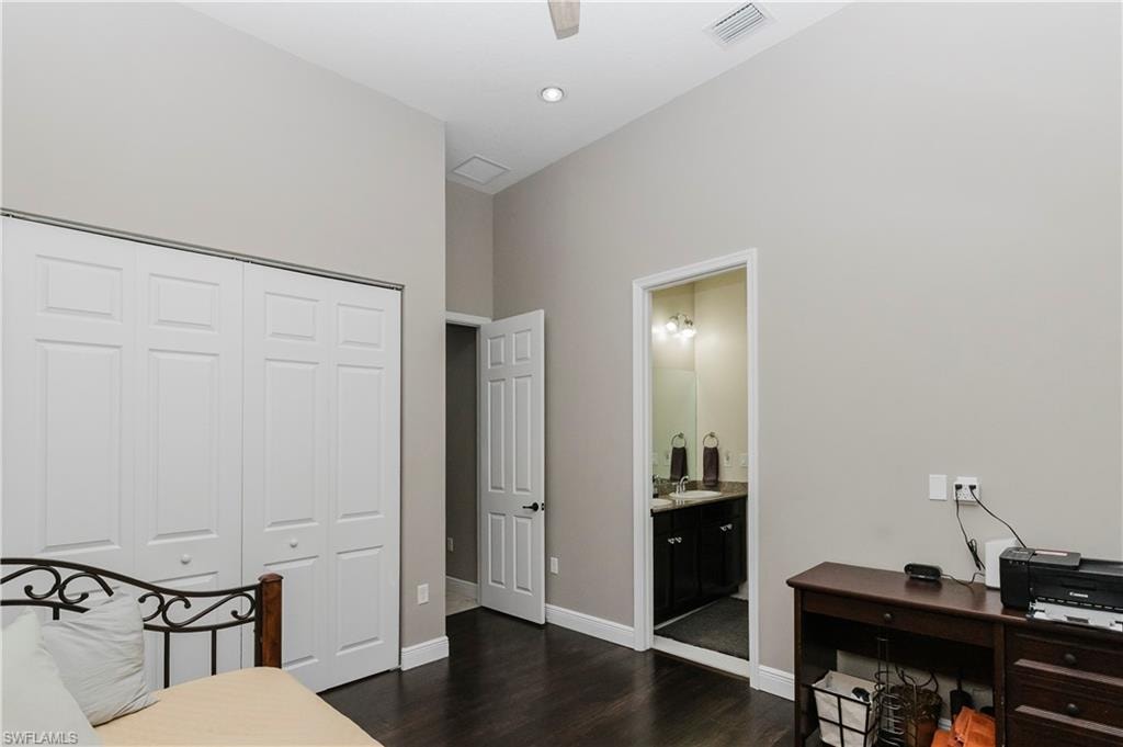Bedroom with an office area, dark wood-style flooring, a closet, a ceiling fan, and ensuite bathroom