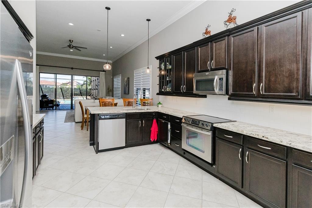 Kitchen with ornamental molding, stainless steel appliances, pendant lighting, tasteful backsplash, and light stone countertops