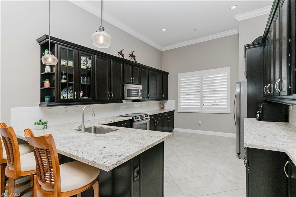 Kitchen with dark cabinetry, backsplash, crown molding, light stone countertops, and a peninsula