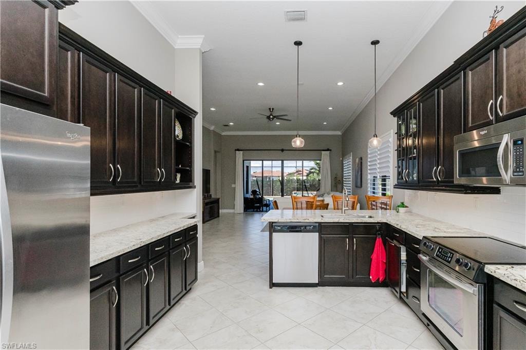 Kitchen with ornamental molding, appliances with stainless steel finishes, light stone countertops, a ceiling fan, and a peninsula