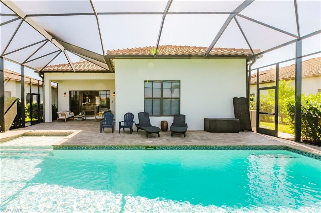 Rear view of house with a sunroom, a patio area, glass enclosure, and a tile roof