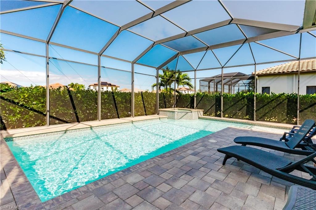 View of swimming pool with a sunroom, glass enclosure, a pool with connected hot tub, and a patio area