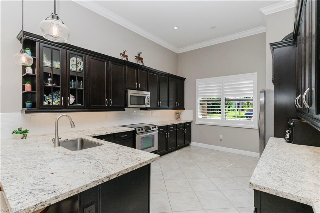 Kitchen with ornamental molding, tasteful backsplash, appliances with stainless steel finishes, light tile patterned flooring, and light stone counters
