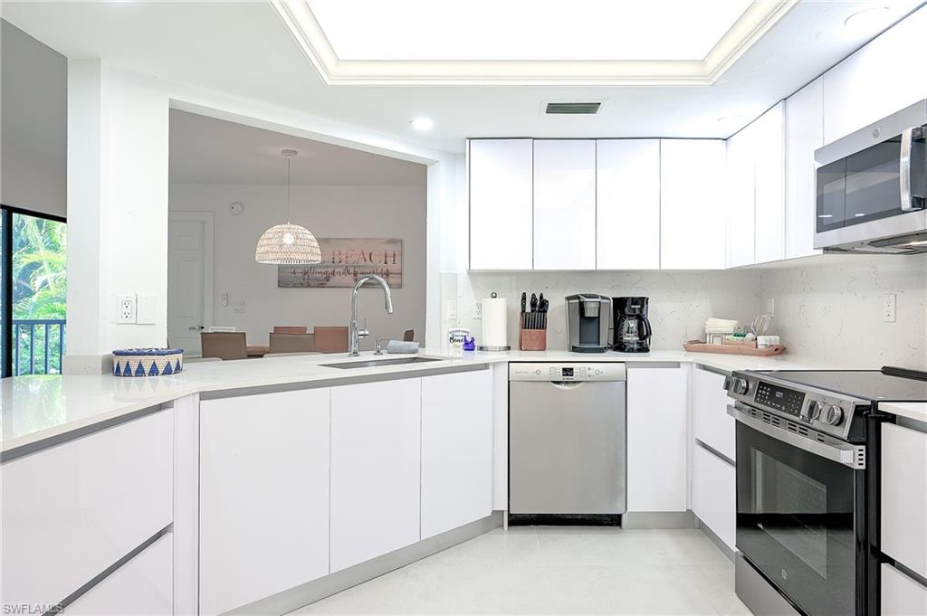Kitchen with appliances with stainless steel finishes, white cabinetry, modern cabinets, decorative backsplash, and hanging light fixtures