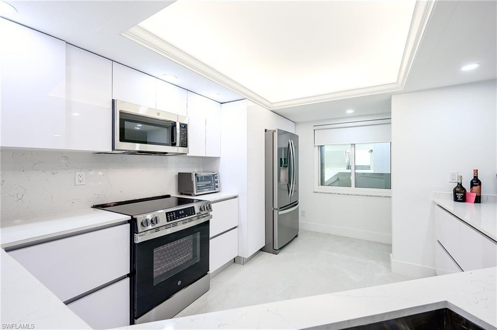 Kitchen featuring white cabinetry, modern cabinets, appliances with stainless steel finishes, tasteful backsplash, and light stone counters