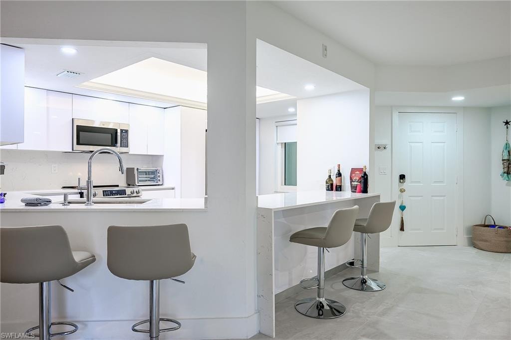 Kitchen with a kitchen breakfast bar, white cabinetry, recessed lighting, a peninsula, and stainless steel microwave