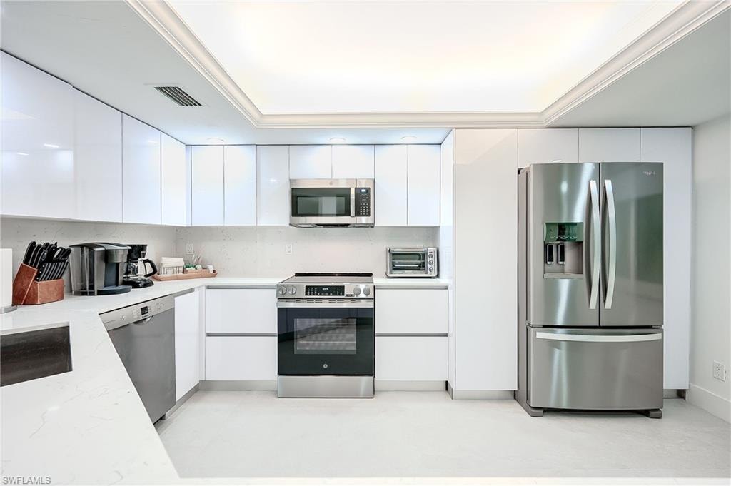 Kitchen featuring stainless steel appliances, white cabinetry, modern cabinets, tasteful backsplash, and light stone countertops
