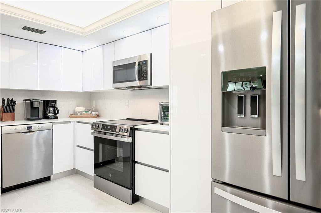Kitchen with modern cabinets, white cabinets, stainless steel appliances, light countertops, and ornamental molding