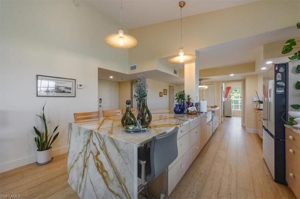 Kitchen with light wood finished floors, decorative light fixtures, modern cabinets, and light stone countertops