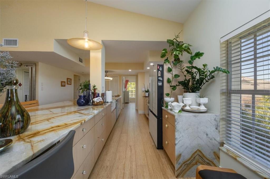 Kitchen featuring hanging light fixtures, light wood-style floors, freestanding refrigerator, light stone countertops, and lofted ceiling