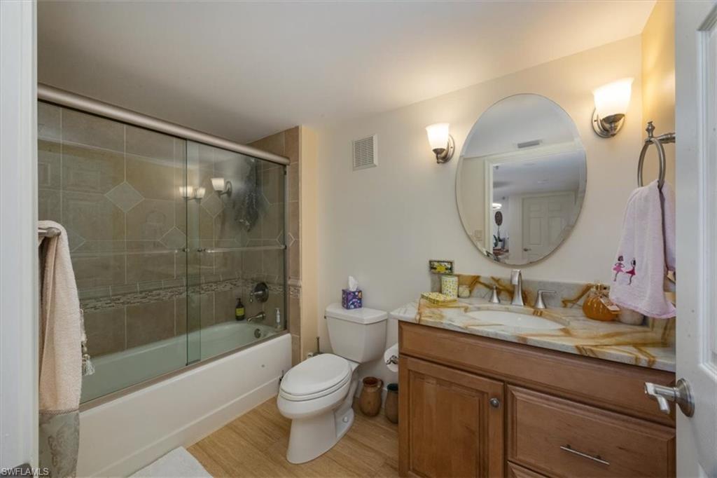 Full bathroom with bath / shower combo with glass door, vanity, and light wood-type flooring