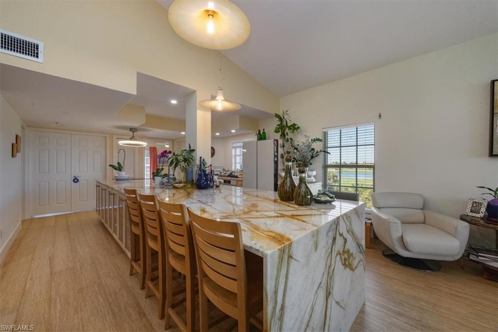 Kitchen featuring light stone counters, lofted ceiling, light wood-type flooring, pendant lighting, and a kitchen bar