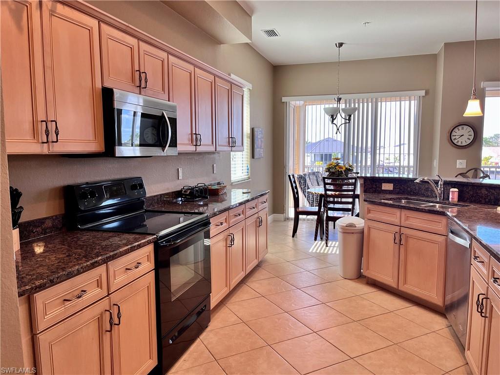 Kitchen with appliances with stainless steel finishes, light tile patterned floors, dark stone counters, and pendant lighting