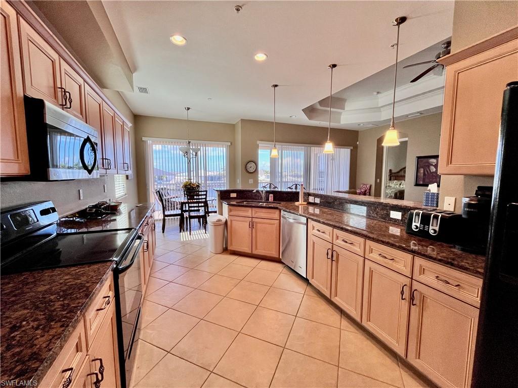 Kitchen featuring stainless steel appliances, hanging light fixtures, light tile patterned floors, dark stone countertops, and a raised ceiling