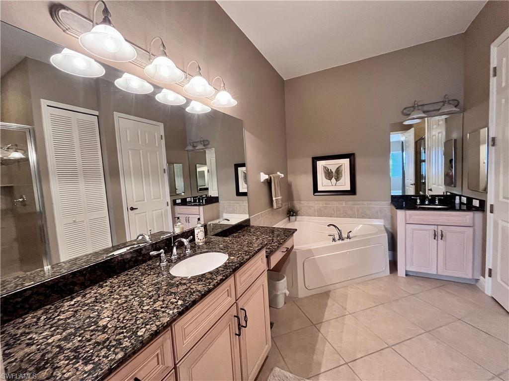 Bathroom featuring two vanities, a closet, light tile patterned flooring, a bath, and a shower stall