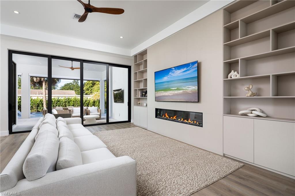 Living area featuring wood finished floors, built in features, a glass covered fireplace, a ceiling fan, and recessed lighting