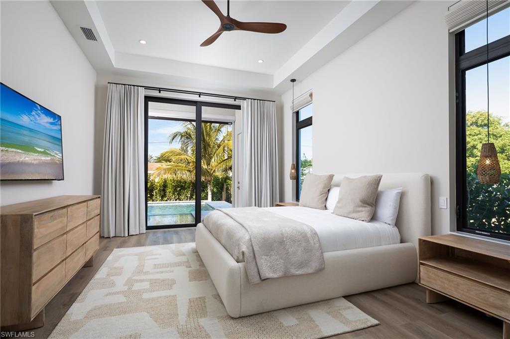 Bedroom featuring wood finished floors, access to exterior, ceiling fan, a tray ceiling, and recessed lighting