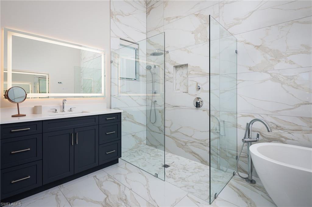 Full bathroom with light marble finish floors, a freestanding bath, vanity, and a marble finish shower