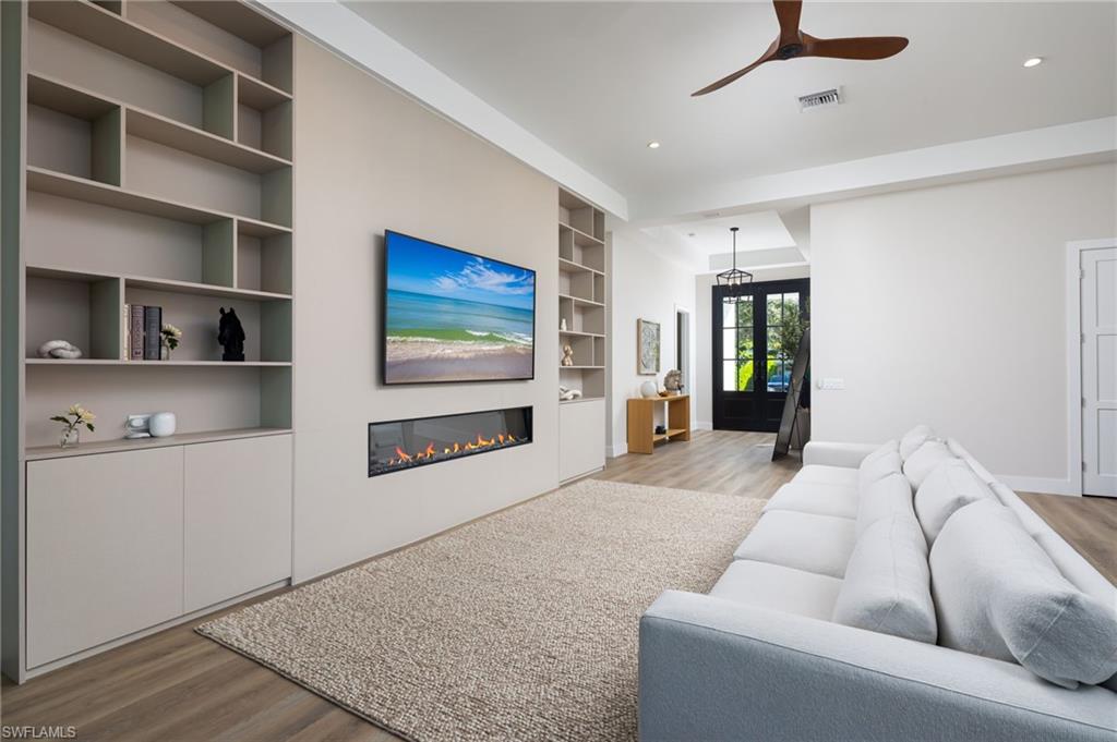 Living room with light wood-style floors, ceiling fan, built in features, a glass covered fireplace, and recessed lighting