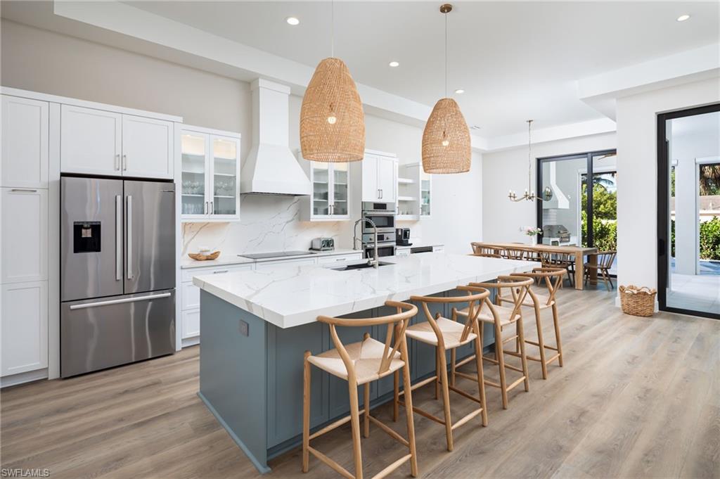 Kitchen with white cabinets, decorative light fixtures, stainless steel appliances, glass insert cabinets, and recessed lighting