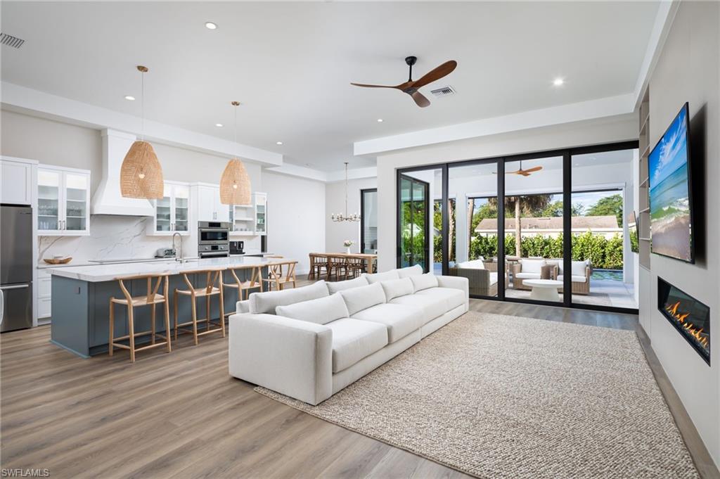 Living area featuring light wood-type flooring, a glass covered fireplace, recessed lighting, a ceiling fan, and a chandelier