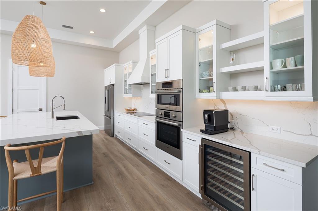 Kitchen featuring white cabinetry, open shelves, wine cooler, light stone counters, and recessed lighting