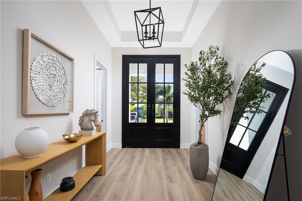 Foyer entrance featuring light wood-style flooring, a tray ceiling, french doors, and a chandelier