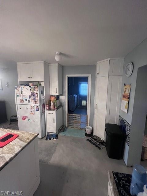 Kitchen with white cabinets, refrigerator, and unfinished concrete floors