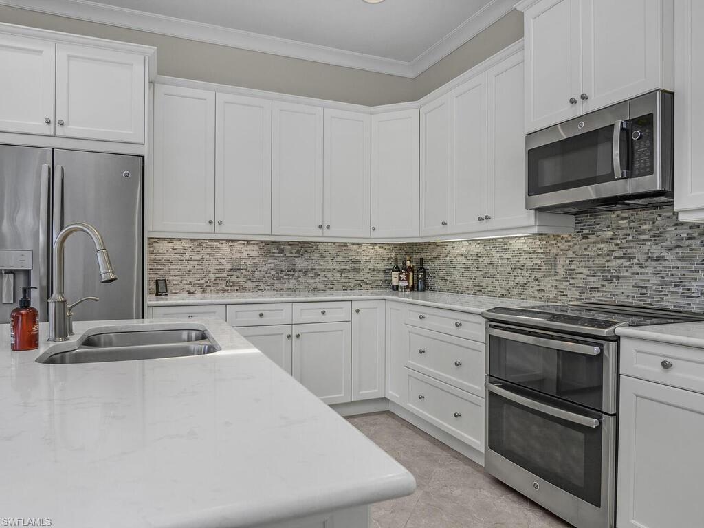 Kitchen with appliances with stainless steel finishes, crown molding, white cabinets, and backsplash, quartz counter tops.