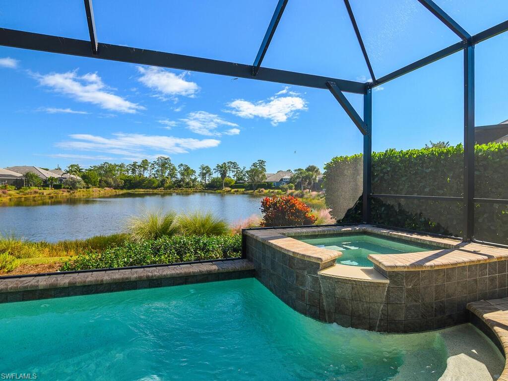View of pool featuring glass enclosure, a sunroom, a water view, and a pool with connected hot tub