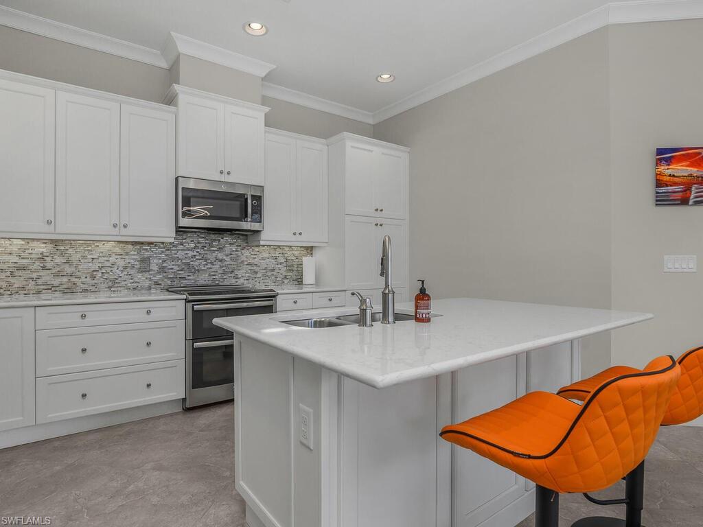 Kitchen with stainless steel appliances, a breakfast bar area, backsplash, ornamental molding, and white cabinetry.