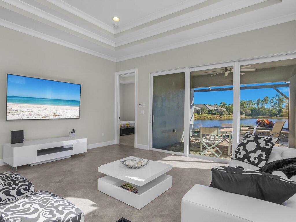 Living room featuring a raised ceiling, ornamental molding, a water view, Lanai, pool and spa views.