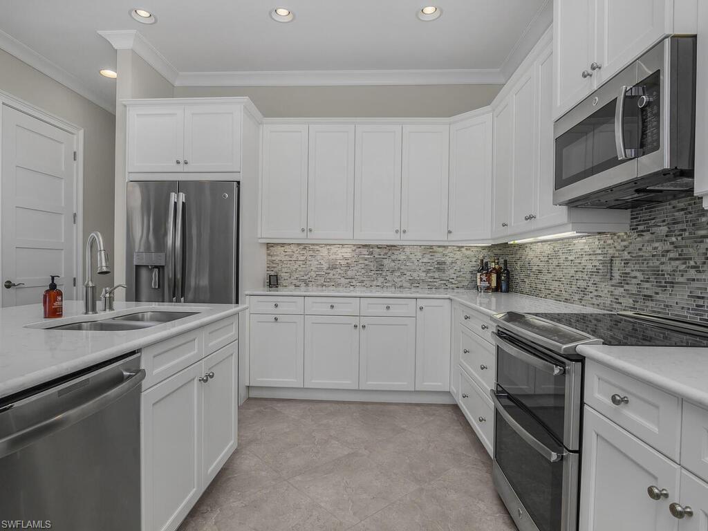 Kitchen with stainless steel appliances, ornamental molding, white cabinets, tasteful backsplash, and recessed lighting. Quartz counter tops.