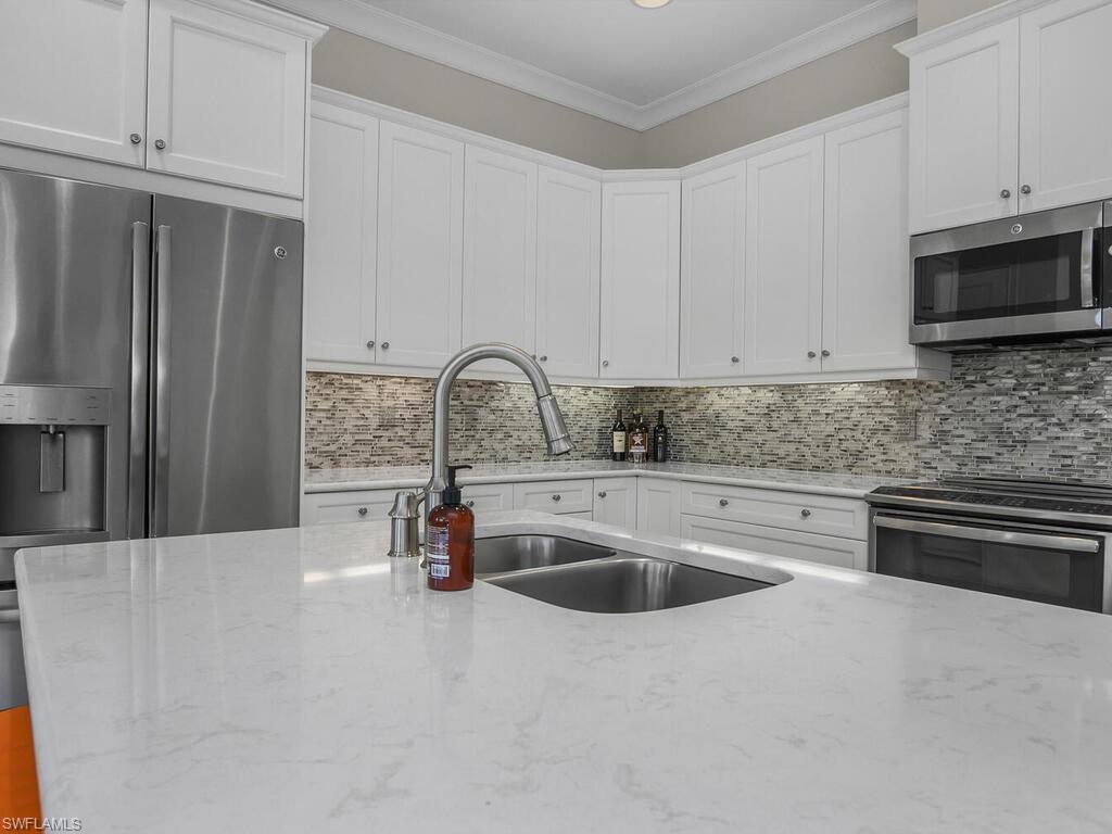 Kitchen with decorative backsplash, appliances with stainless steel finishes, light quartz countertops, ornamental molding, and white cabinets.