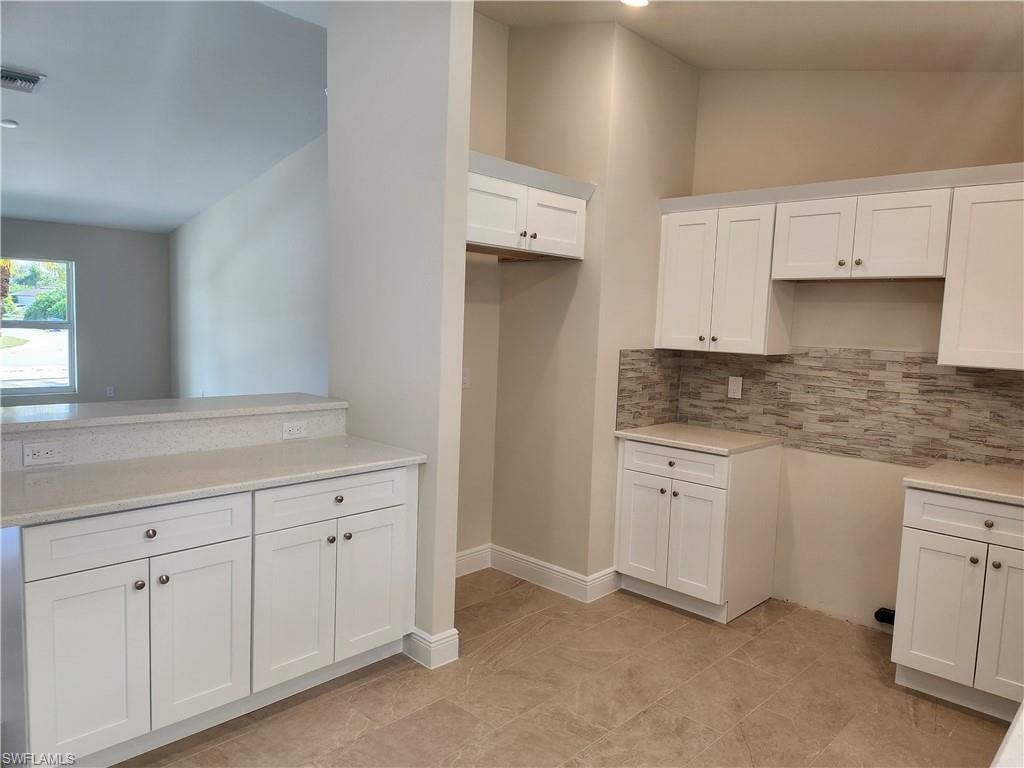 Kitchen featuring white cabinetry, backsplash, and light stone countertops