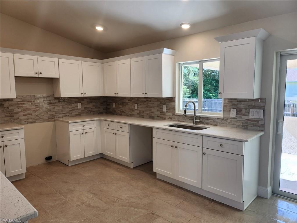 Kitchen featuring white cabinetry, light stone counters, tasteful backsplash, lofted ceiling, and recessed lighting