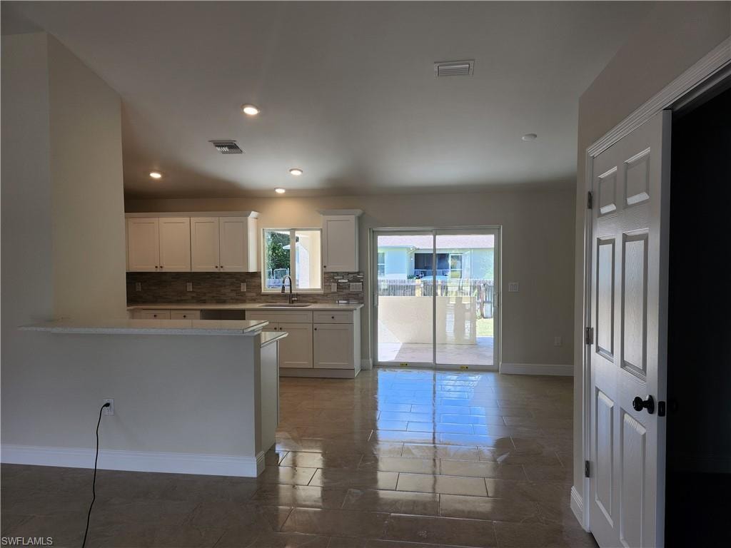 Kitchen featuring tasteful backsplash, white cabinetry, recessed lighting, light stone counters, and dark tile patterned floors