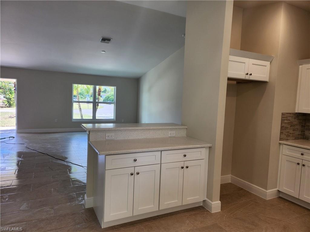 Kitchen featuring white cabinetry, light stone countertops, a peninsula, and open floor plan