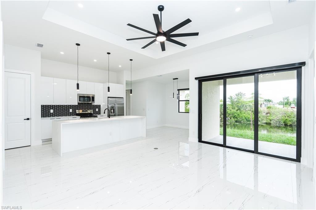Kitchen with a tray ceiling, backsplash, a center island with sink, stainless steel appliances, and recessed lighting