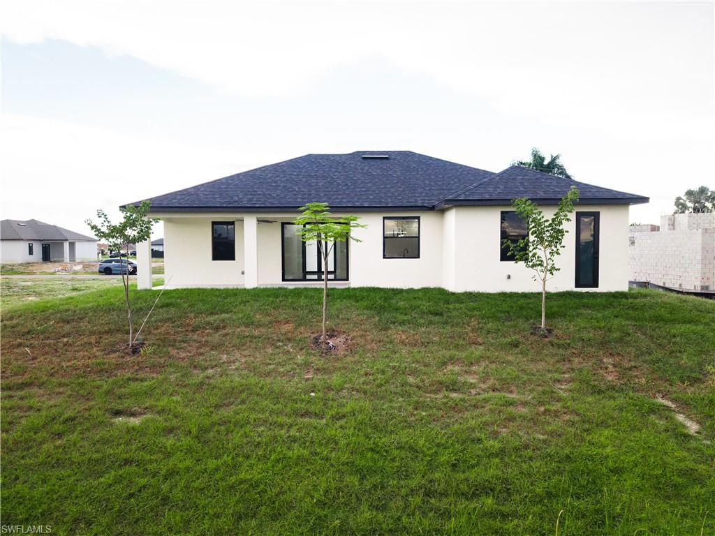 Back of property with stucco siding, a yard, a shingled roof, and a patio area