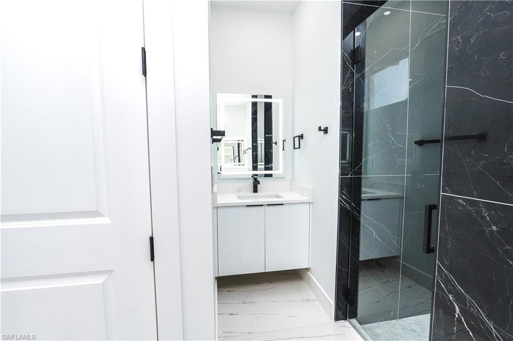 Full bathroom with vanity, a marble finish shower, and light marble finish flooring