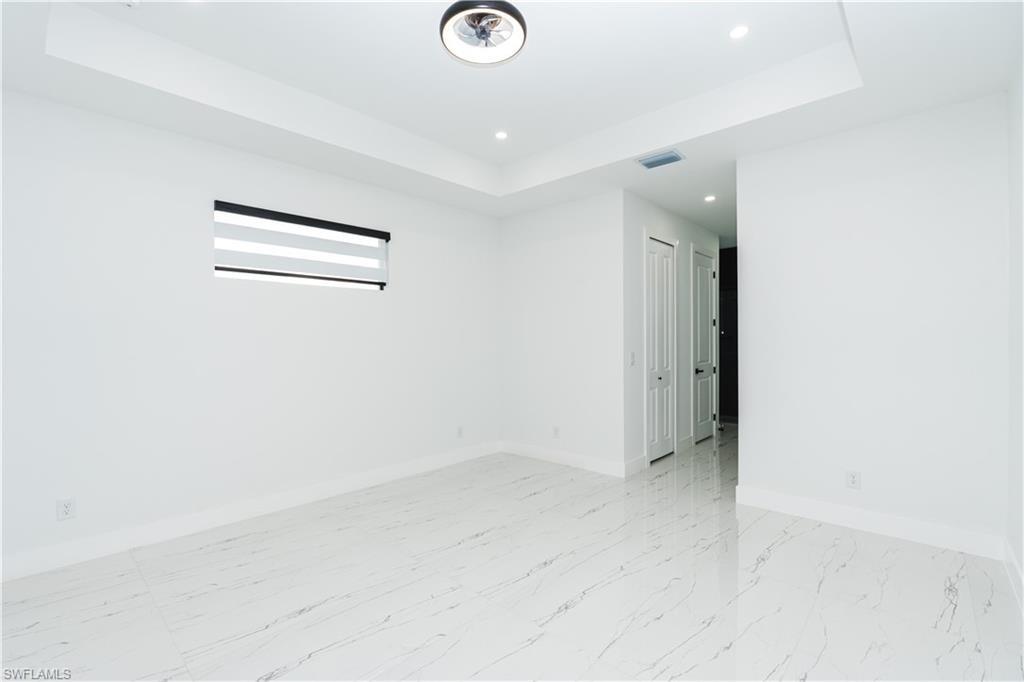 Spare room featuring a raised ceiling, light marble finish flooring, and recessed lighting