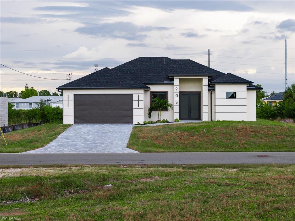 Prairie-style home with decorative driveway, a front yard, stucco siding, and an attached garage