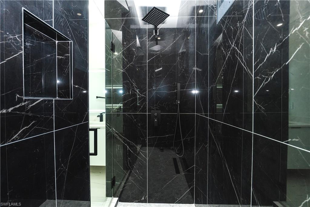 Bathroom with vanity, a marble finish shower, and light marble finish floors