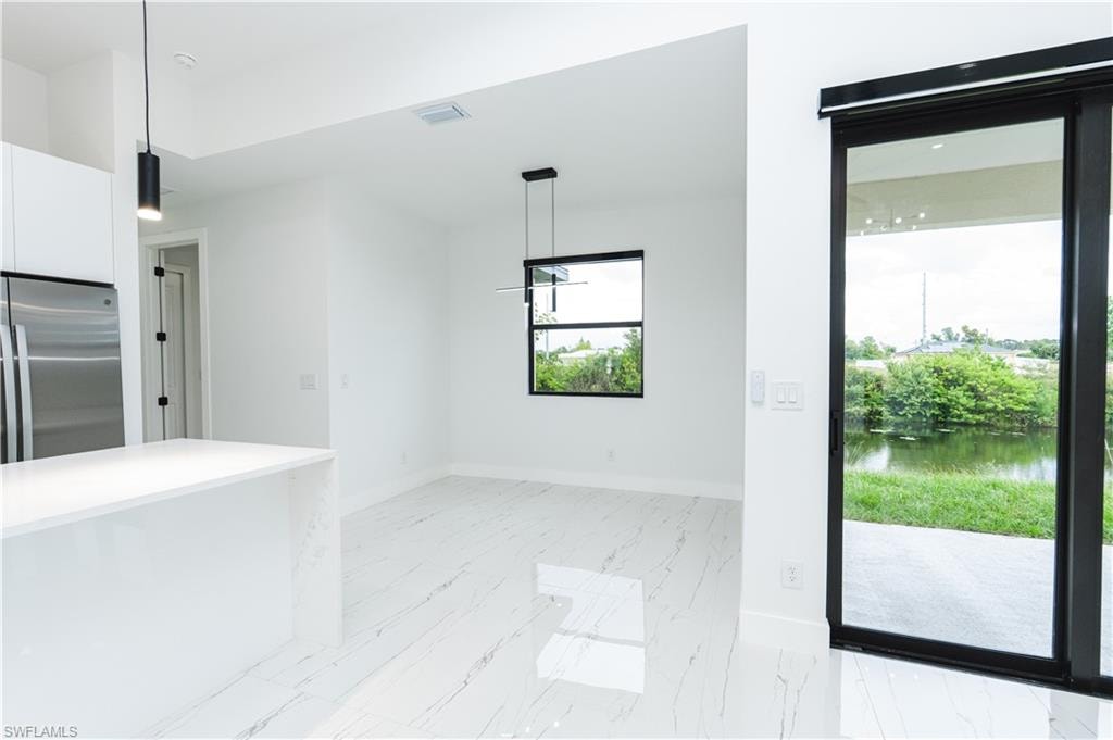 Kitchen with appliances with stainless steel finishes, tasteful backsplash, a kitchen island with sink, light stone counters, and decorative light fixtures