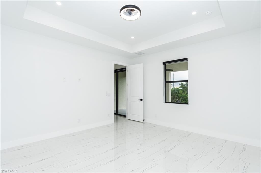 Empty room featuring a tray ceiling, recessed lighting, and light marble finish floors