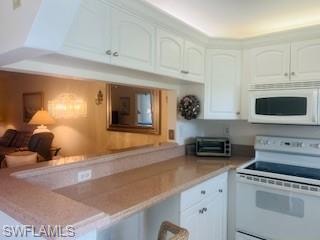Kitchen with white appliances, white cabinetry, light countertops, and a peninsula